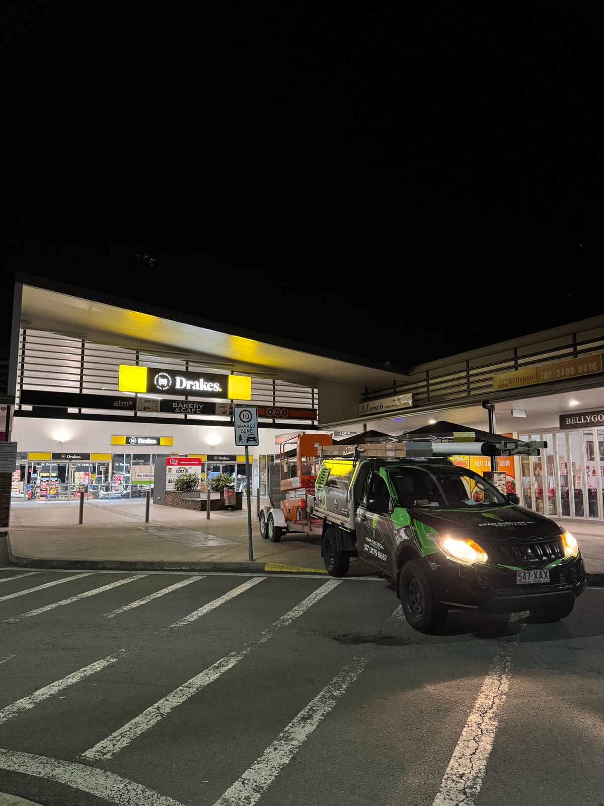 Egan Electrical ute towing a scissor lift at a shopping centre at night